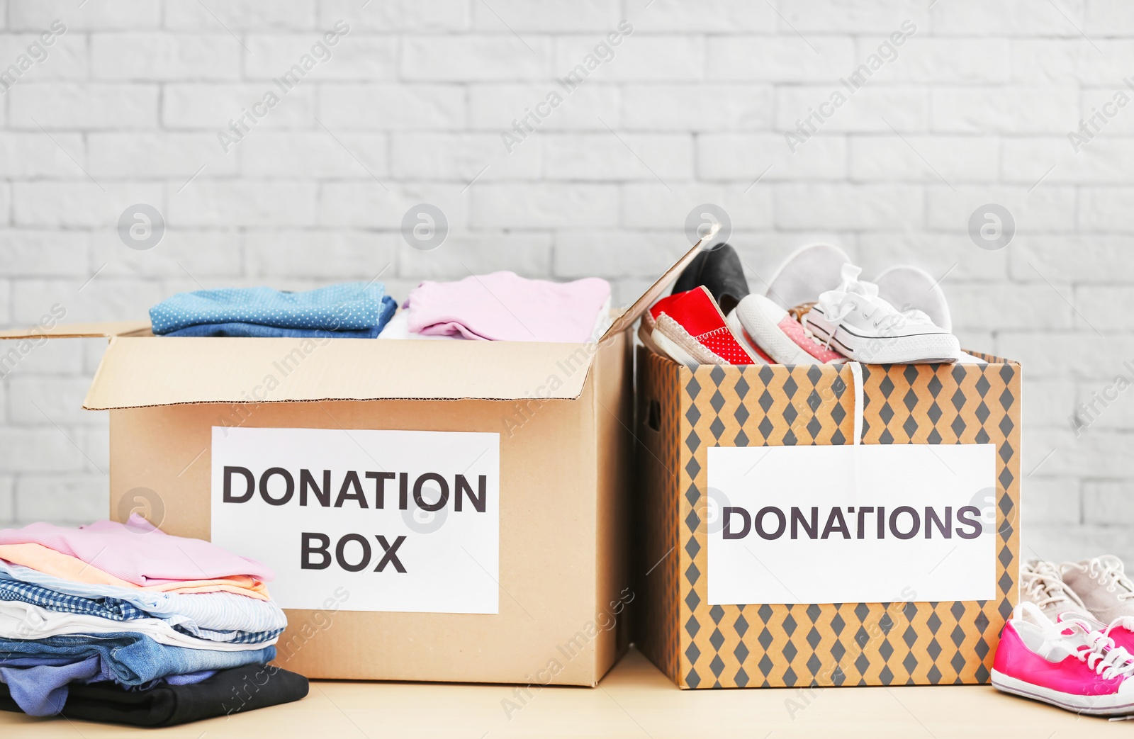 Photo of Donation boxes with clothes and shoes on table against brick wall