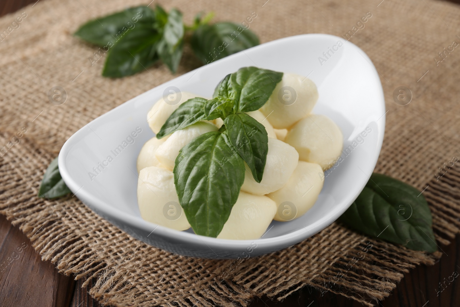 Photo of Tasty mozarella balls and basil leaves in bowl on table, closeup