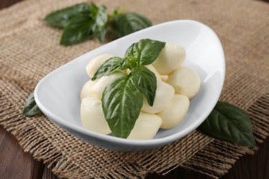 Tasty mozarella balls and basil leaves in bowl on table, closeup