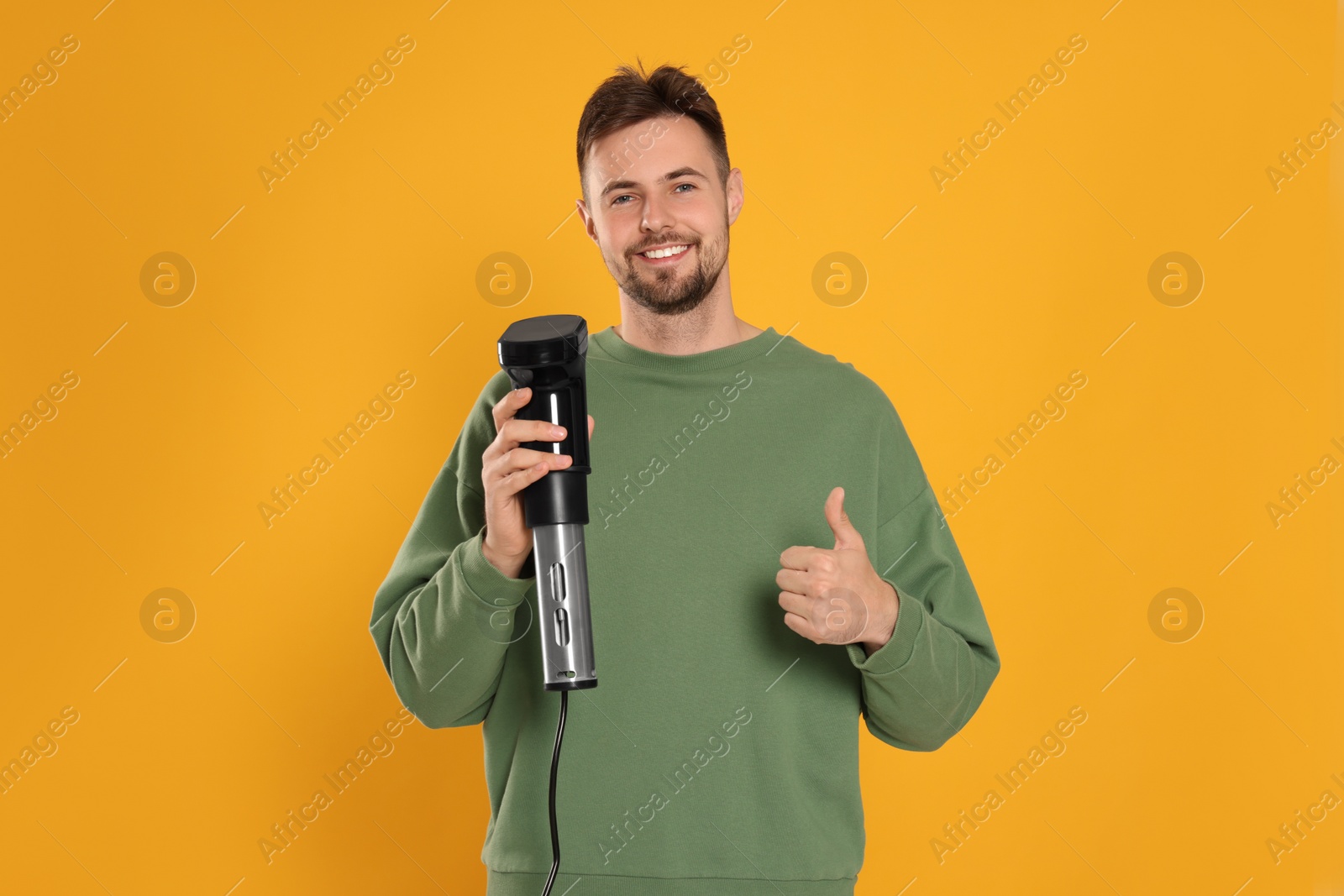 Photo of Smiling man holding sous vide cooker and showing thumb up on orange background