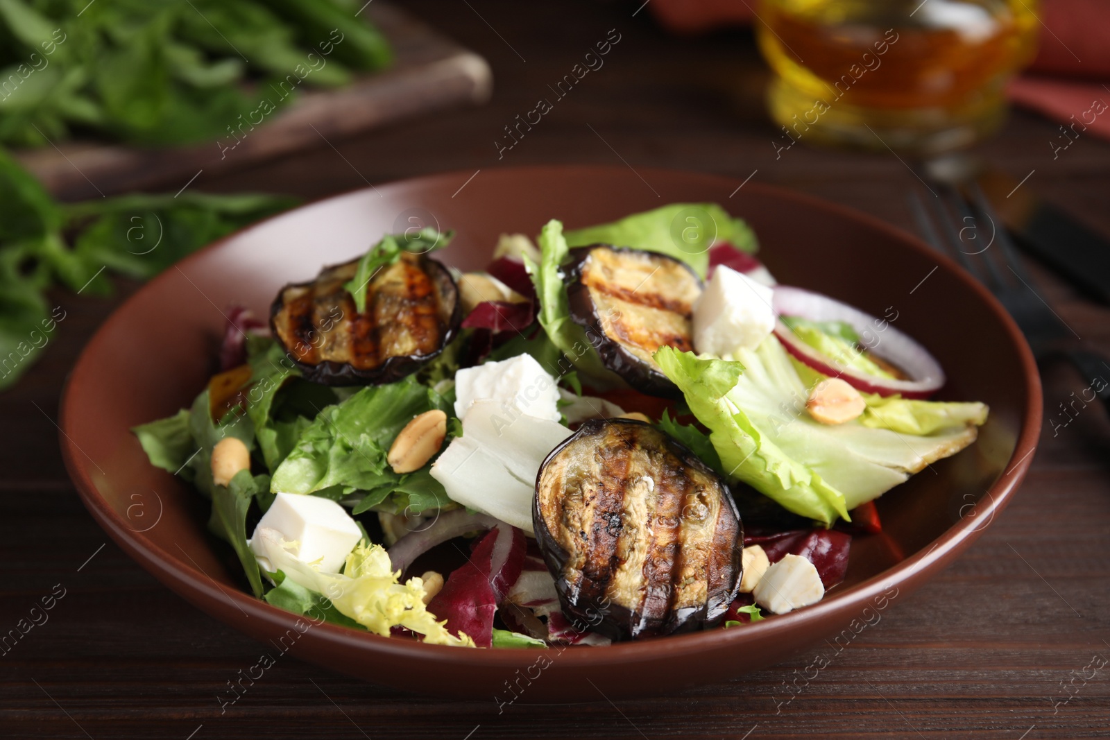 Photo of Delicious salad with roasted eggplant, feta cheese and arugula served on wooden table, closeup