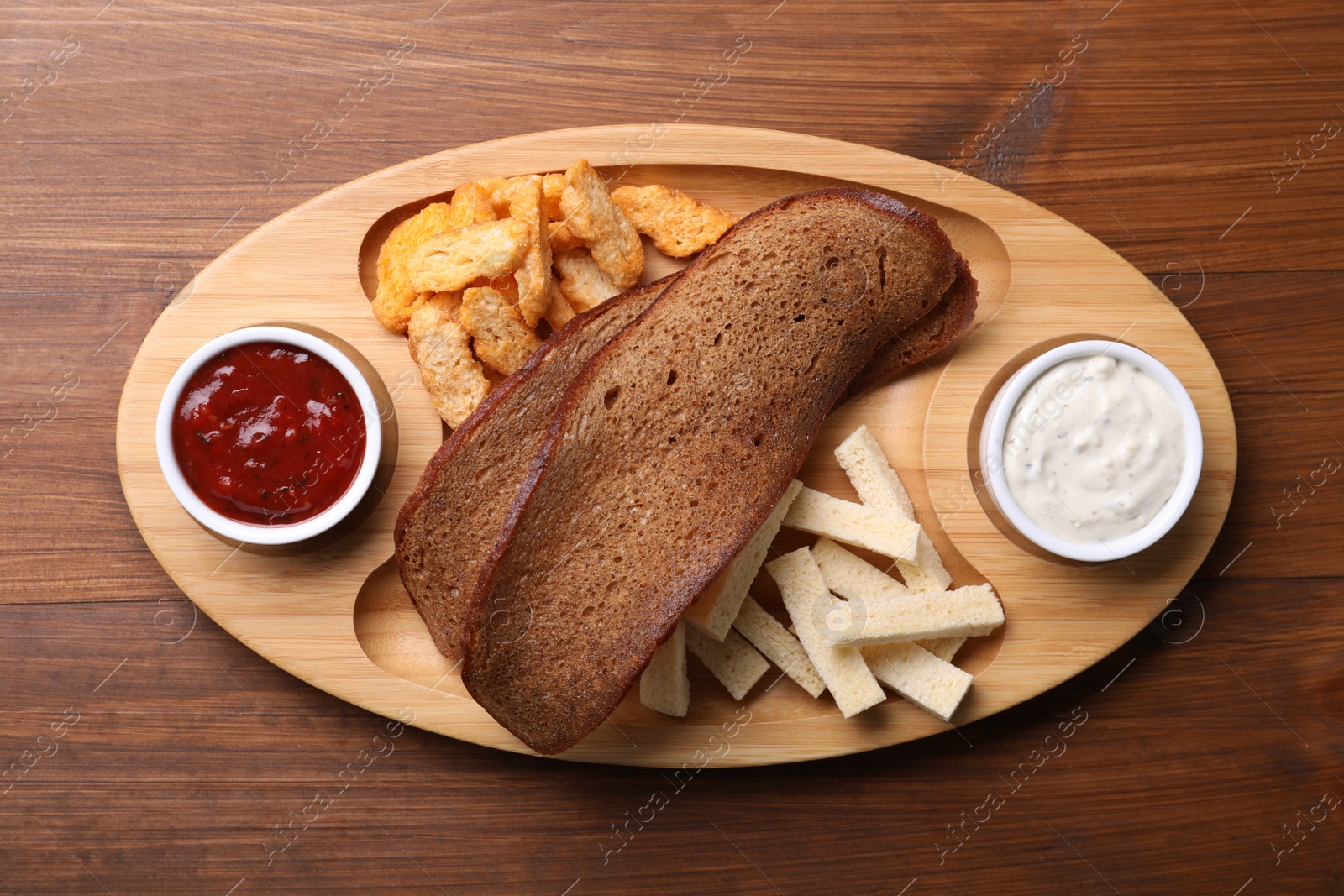 Photo of Tray with different crispy rusks and dip sauces on wooden table, top view