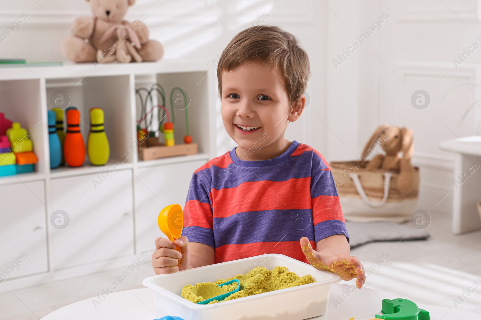 Photo of Cute little boy playing with bright kinetic sand at table in room