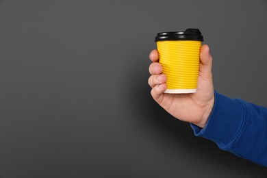 Man holding takeaway cup with drink on dark grey background, closeup view and space for text. Coffee to go