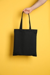 Man holding cotton shopping eco bag on color background. Mockup for design