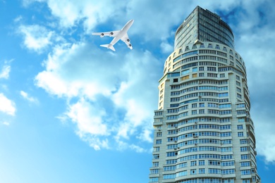 Image of Airplane flying in blue sky over skyscraper