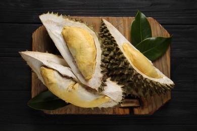 Photo of Pieces of fresh ripe durian on black wooden table, top view