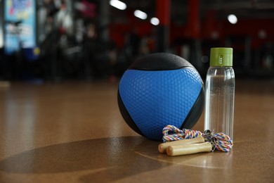 Photo of Medicine ball, bottle and skipping rope on floor in gym. Space for text