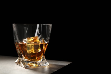 Golden whiskey in glass with ice cubes on table. Space for text