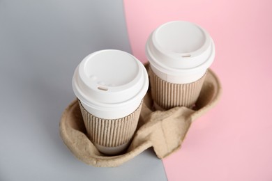 Takeaway paper coffee cups with sleeves and plastic lids in cardboard holder on color background