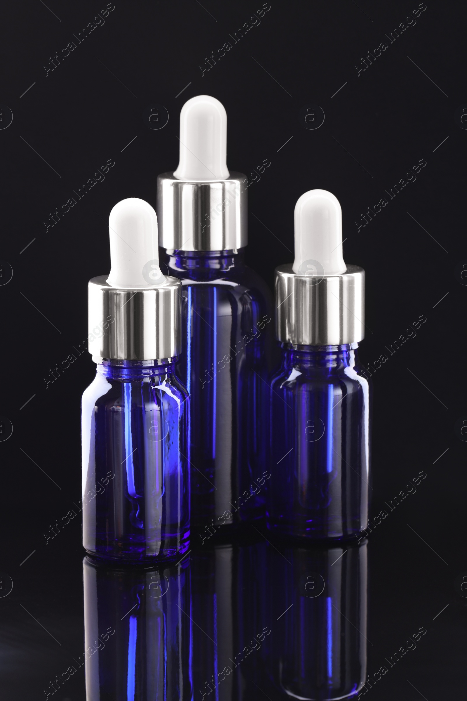 Photo of Tincture in bottles on mirror table against dark background