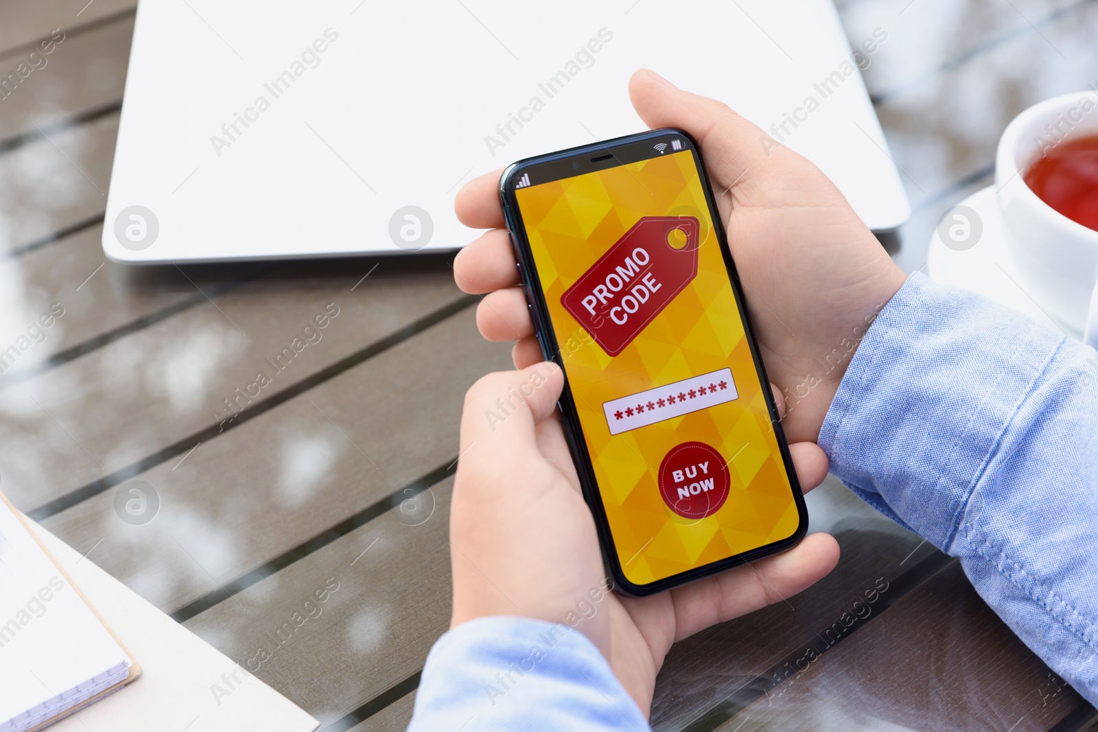 Photo of Man holding smartphone with promo code at wooden table outdoors, closeup