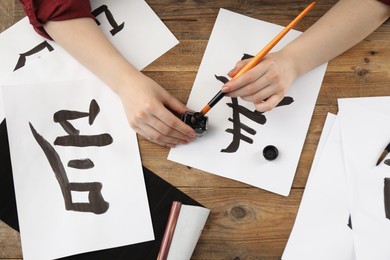 Calligraphy. Woman with brush and inkwell writing hieroglyphs on paper at wooden table, top view