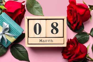 Wooden block calendar with date 8th of March, roses and gift box on pink background, flat lay. International Women's Day