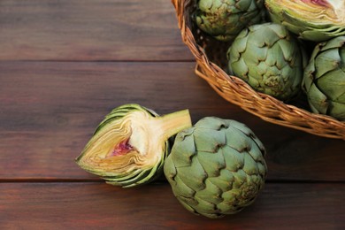 Photo of Wicker basket with fresh raw artichokes on wooden table