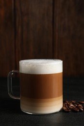 Photo of Glass cup of delicious layered coffee and beans on black table against wooden background, space for text