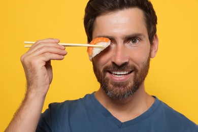 Photo of Funny man holding sushi with chopsticks on orange background