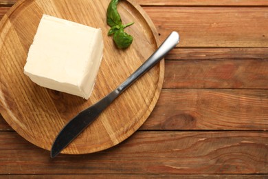 Block of tasty butter, knife and basil on wooden table, top view. Space for text