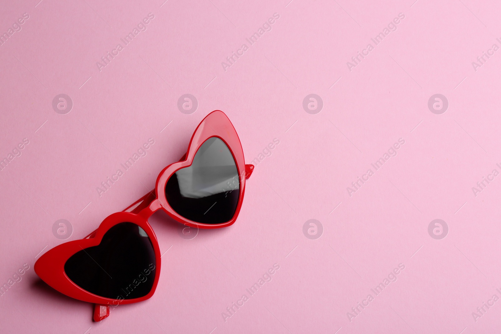 Photo of Stylish heart shaped sunglasses on pink background, top view with space for text. Fashionable accessory