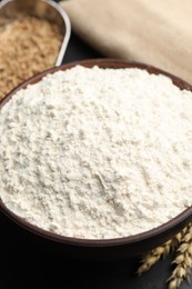 Photo of Wheat flour in bowl on black table, closeup