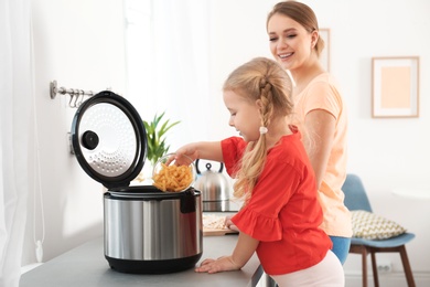 Mother and daughter preparing pasta with modern multi cooker in kitchen