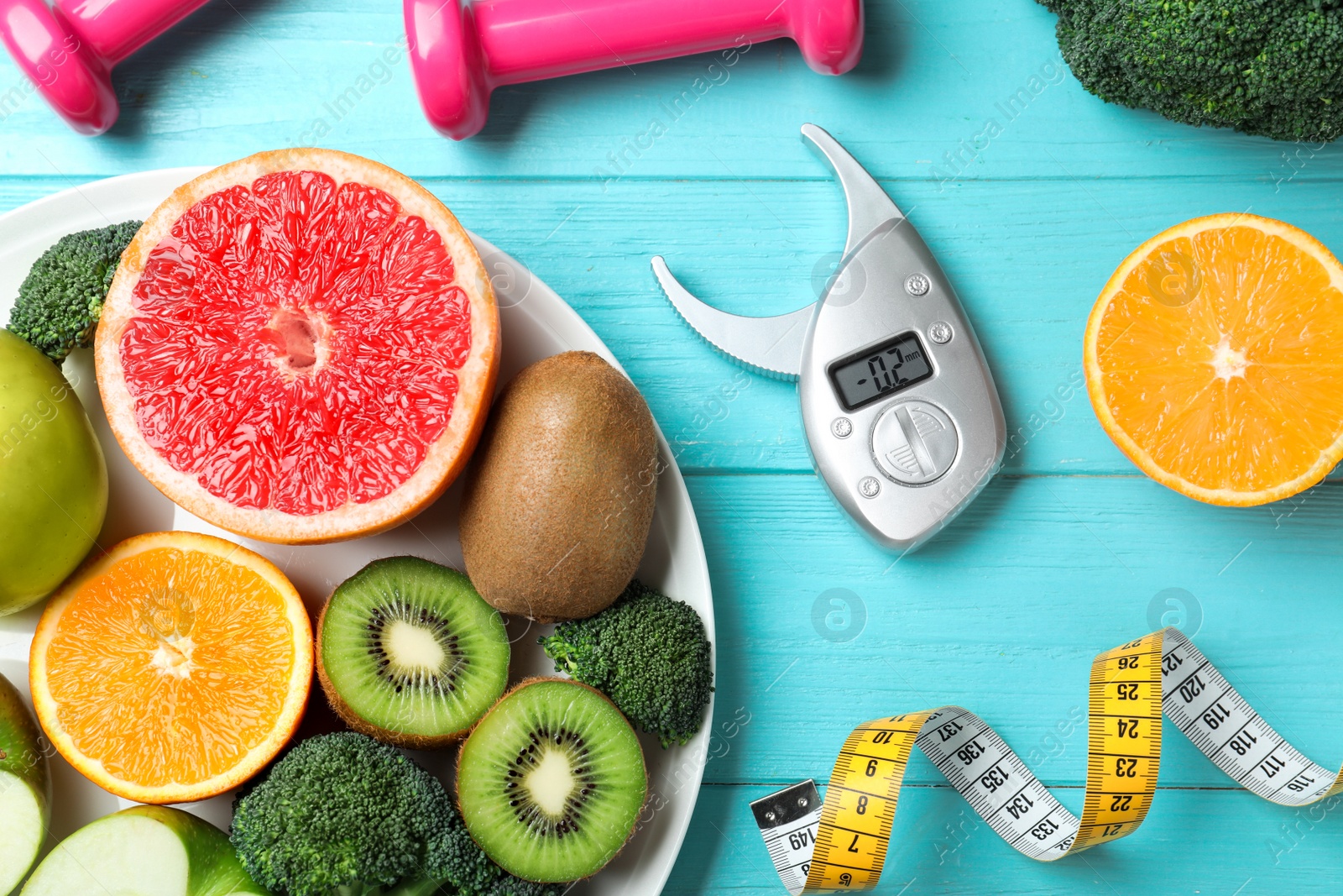 Photo of Fruits, vegetables, measuring tape, digital caliper and dumbbells on light blue wooden background, flat lay. Visiting nutritionist