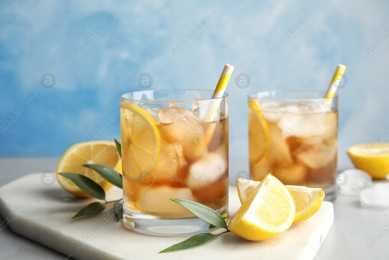 Photo of Glasses of lemonade with ice cubes and fruit on table against color background