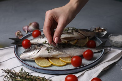 Woman adding spices onto raw dorado fish at grey table, closeup