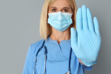 Doctor in protective mask showing stop gesture on grey background. Prevent spreading of coronavirus