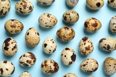 Photo of Speckled quail eggs on light blue background, flat lay