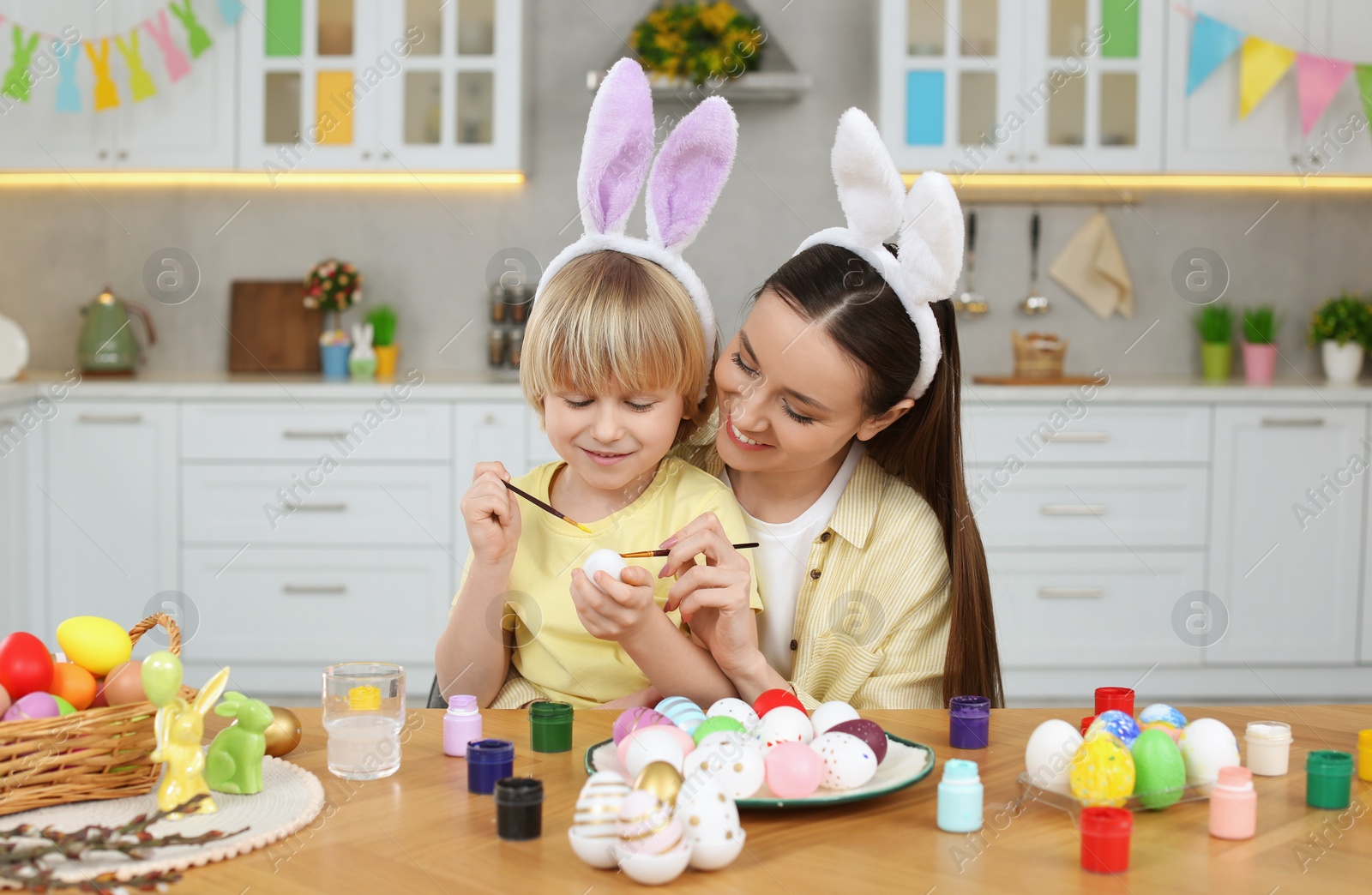 Photo of Mother and her cute son painting Easter eggs at table in kitchen