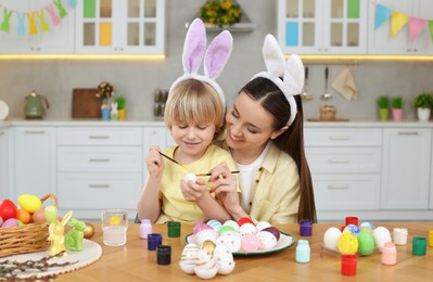 Photo of Mother and her cute son painting Easter eggs at table in kitchen