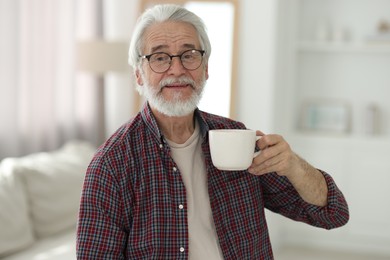 Portrait of happy grandpa with glasses and cup of drink indoors