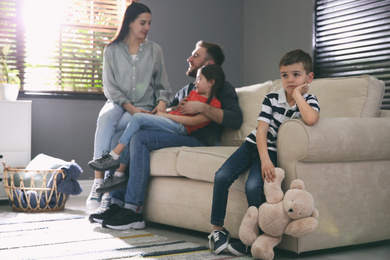 Unhappy little boy feeling jealous while parents spending time with his sister at home