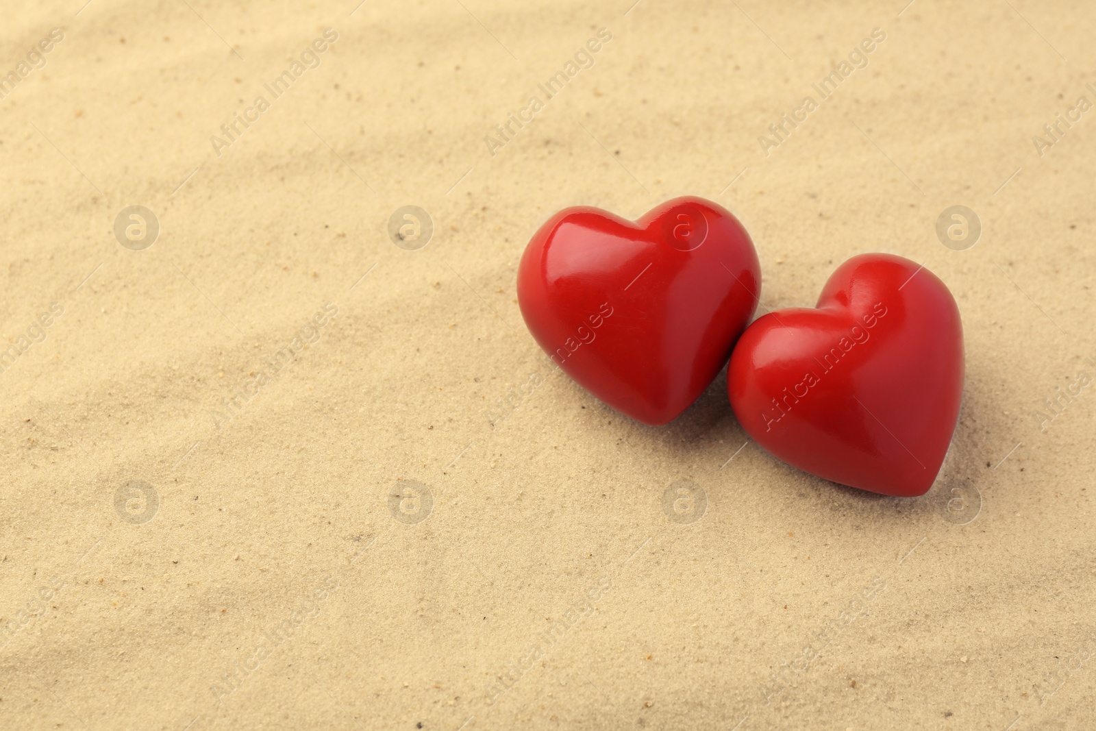 Photo of Honeymoon concept. Two red wooden hearts on sand, space for text