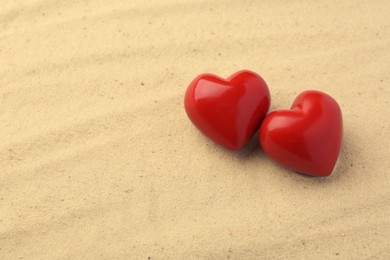 Photo of Honeymoon concept. Two red wooden hearts on sand, space for text