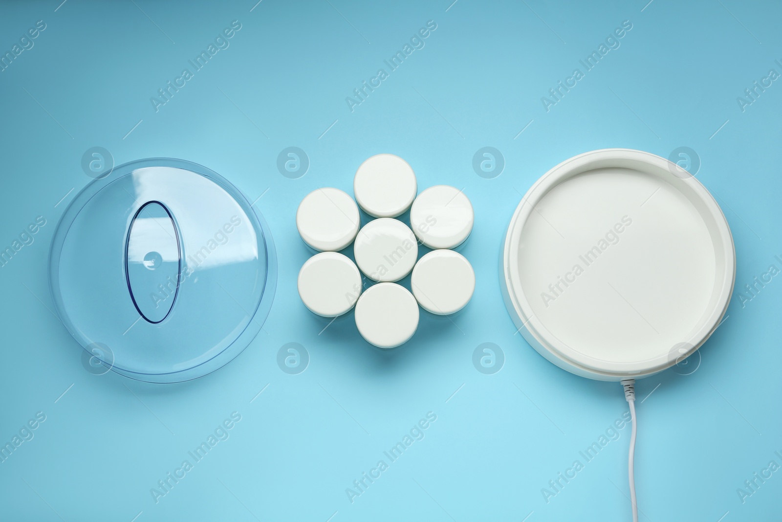 Photo of Modern yogurt maker and jars on light blue background, flat lay