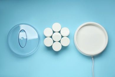 Modern yogurt maker and jars on light blue background, flat lay