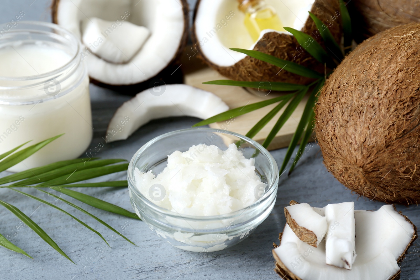 Photo of Organic coconut cooking oil, leaves and fresh fruits on grey wooden table, closeup