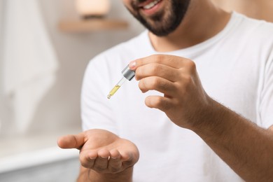 Photo of Young man applying cosmetic serum onto his hand indoors, closeup