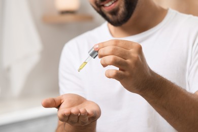 Young man applying cosmetic serum onto his hand indoors, closeup