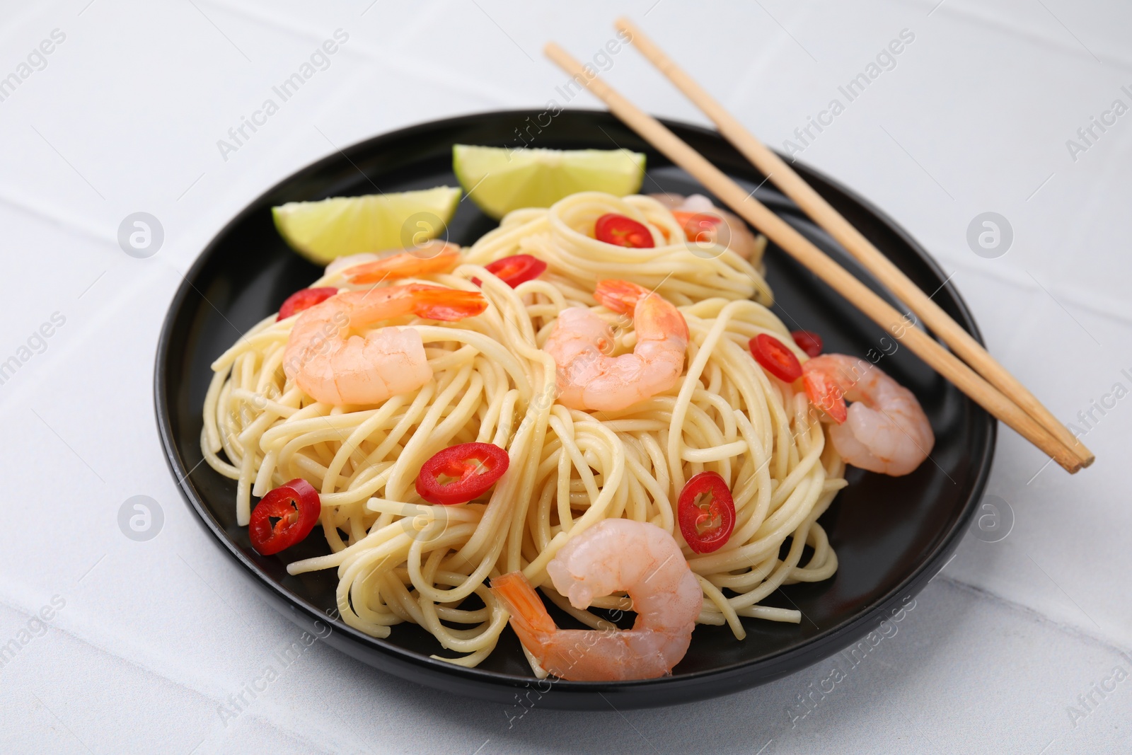 Photo of Tasty spaghetti with shrimps, chili pepper and lime on light tiled table, closeup