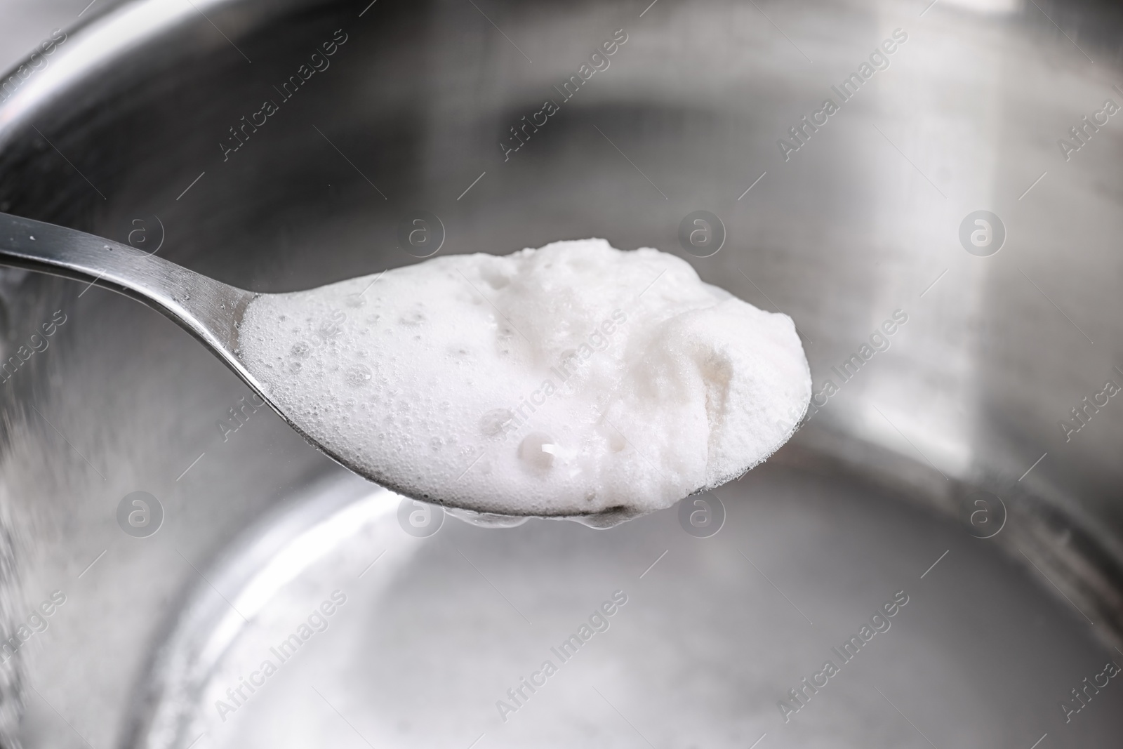 Photo of Chemical reaction of vinegar and baking soda in spoon over saucepan, closeup