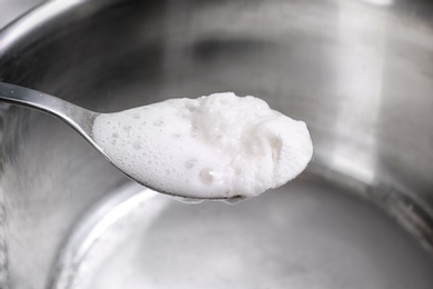 Photo of Chemical reaction of vinegar and baking soda in spoon over saucepan, closeup