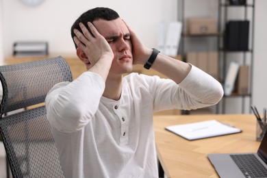 Photo of Young man suffering from headache at workplace in office