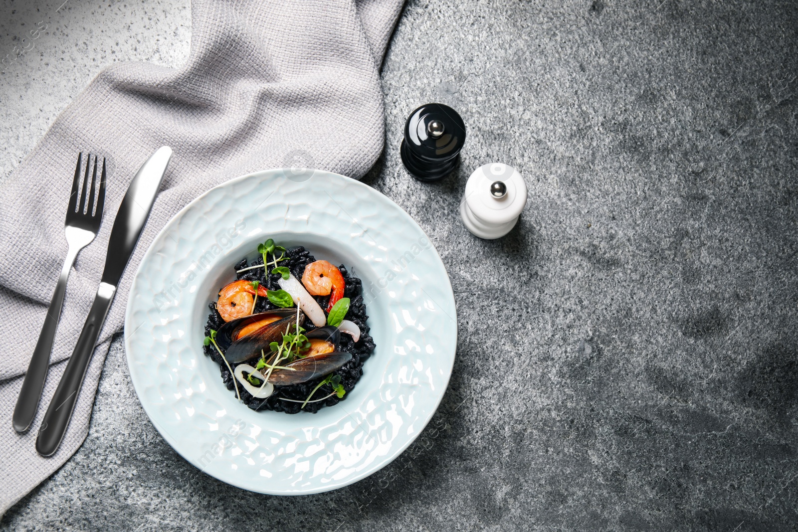 Photo of Delicious black risotto with seafood served on grey table, flat lay. Space for text