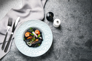 Delicious black risotto with seafood served on grey table, flat lay. Space for text