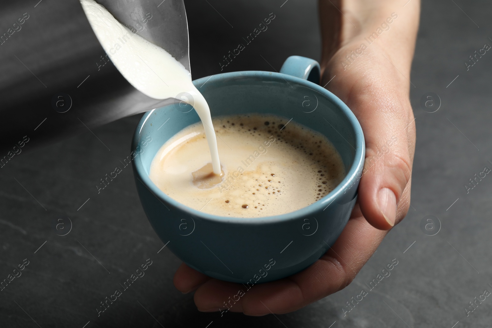 Photo of Woman pouring milk into cup of coffee at black table, closeup