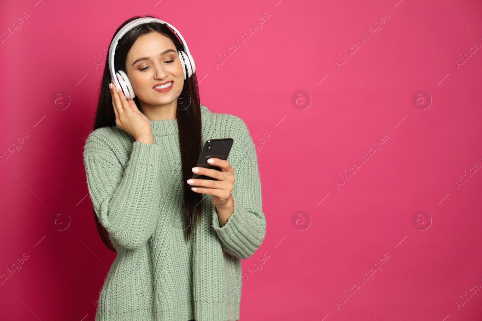 Photo of Young woman listening to audiobook on pink background. Space for text