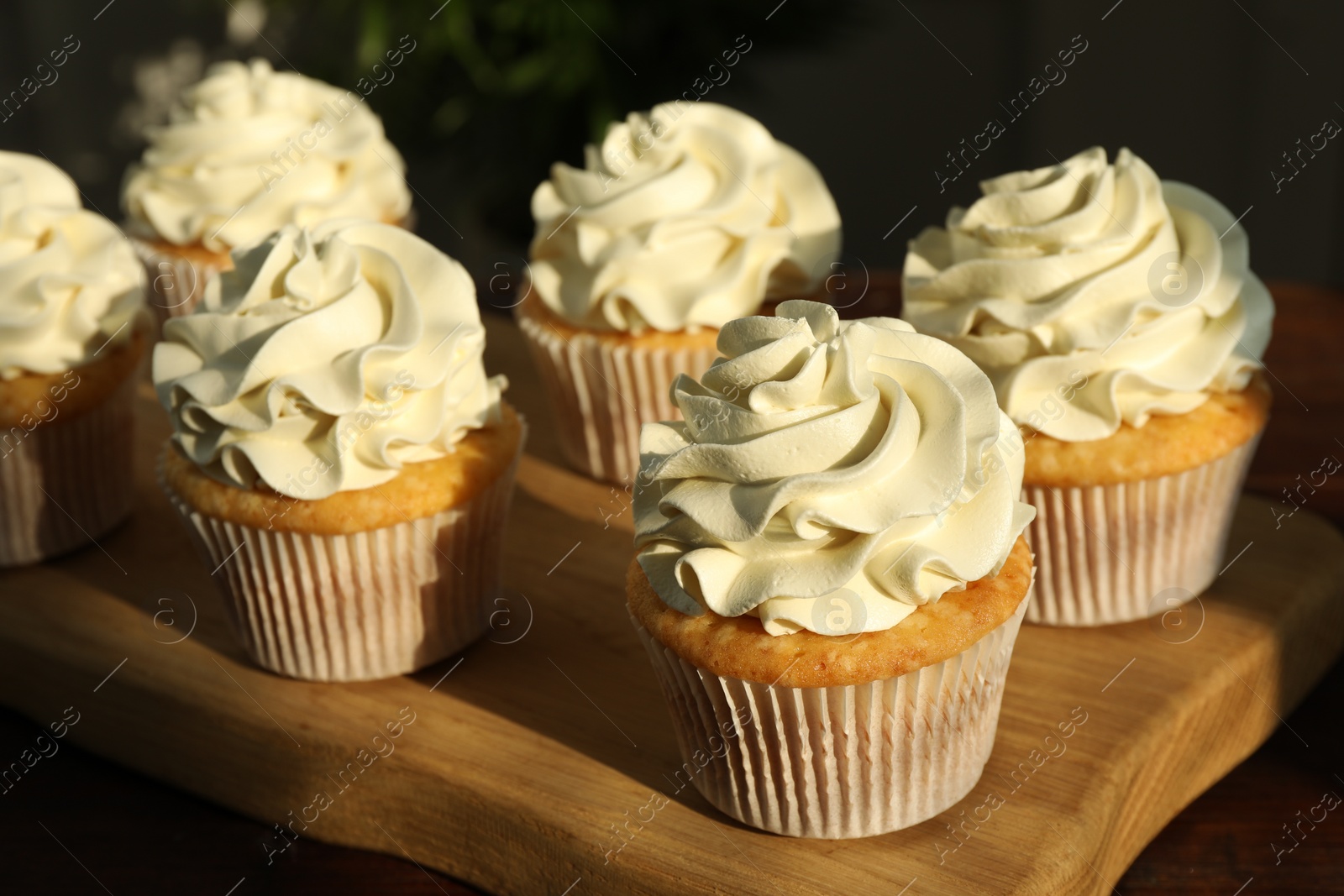 Photo of Tasty cupcakes with vanilla cream on wooden table, closeup